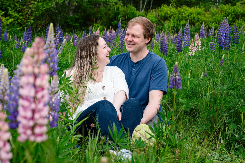 A couple sitting in a field of colorful lupin flowers, smiling and enjoying each other's company.