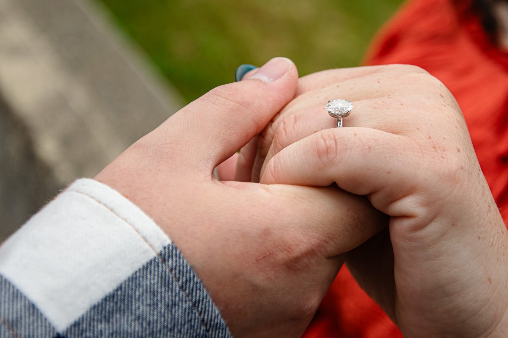 Two hands holding each other, with one hand displaying an engagement ring.