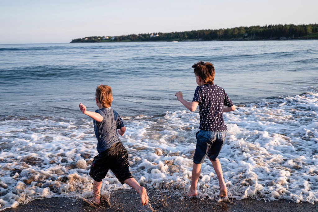 Two young boys running along the beach, playing in the shallow waves of the ocean during sunset.