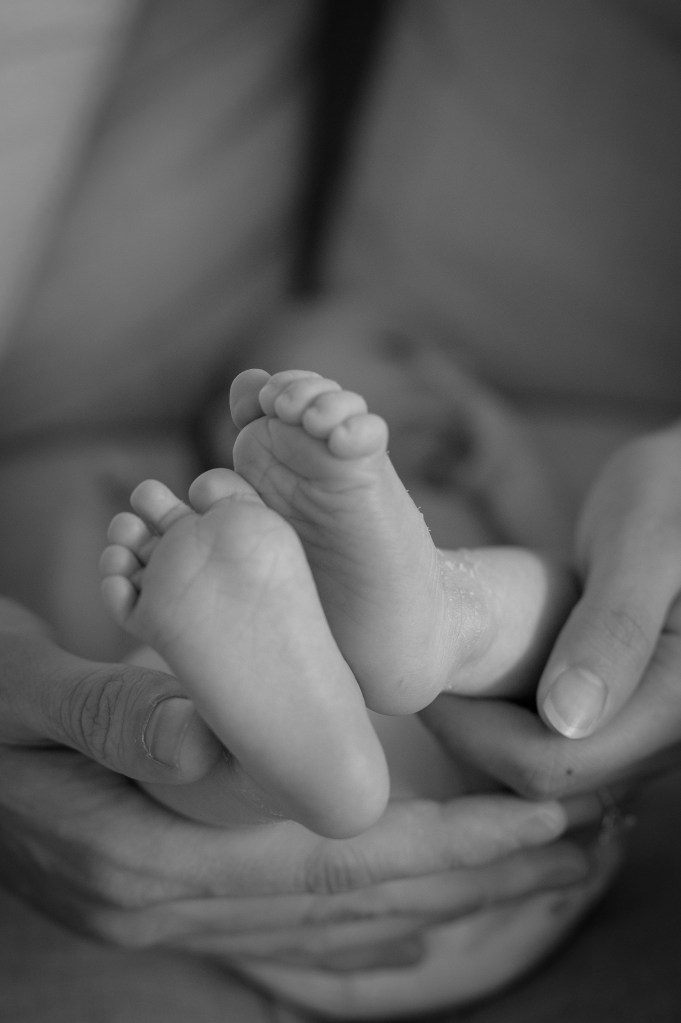 Close-up of a person's hands gently holding a baby's feet, showcasing the tiny toes and soft skin.