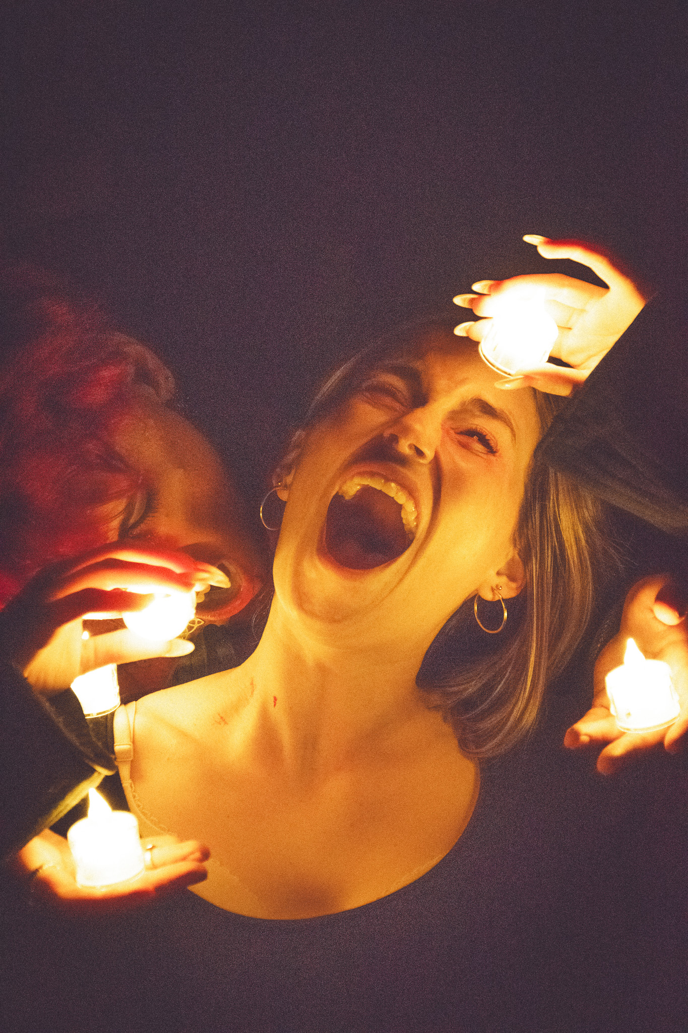A woman with a joyful expression surrounded by illuminated candle-like objects, with other hands appearing from the shadows.